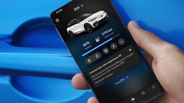 Gros plan d’une main tenant un téléphone intelligent devant la poignée de porte d’une Acura bleue. L’écran du téléphone intelligent affiche une Acura avec les phares allumés et la phrase « Acura. Conduisez comme jamais auparavant. »