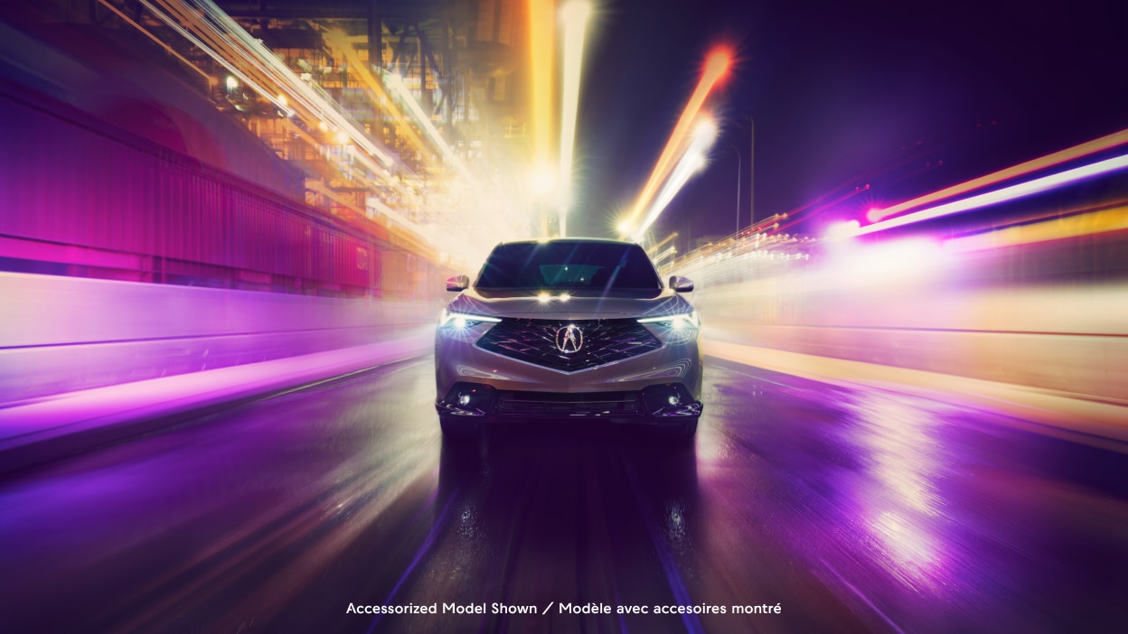 Acura ADX vu de l’avant sur une rue urbaine avec un effet de lumières floues en arrière-plan.