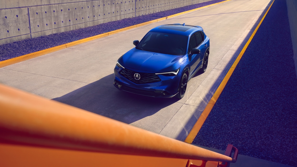 Plan grand angle en plongée d’un Acura ADX bleu sur une route.