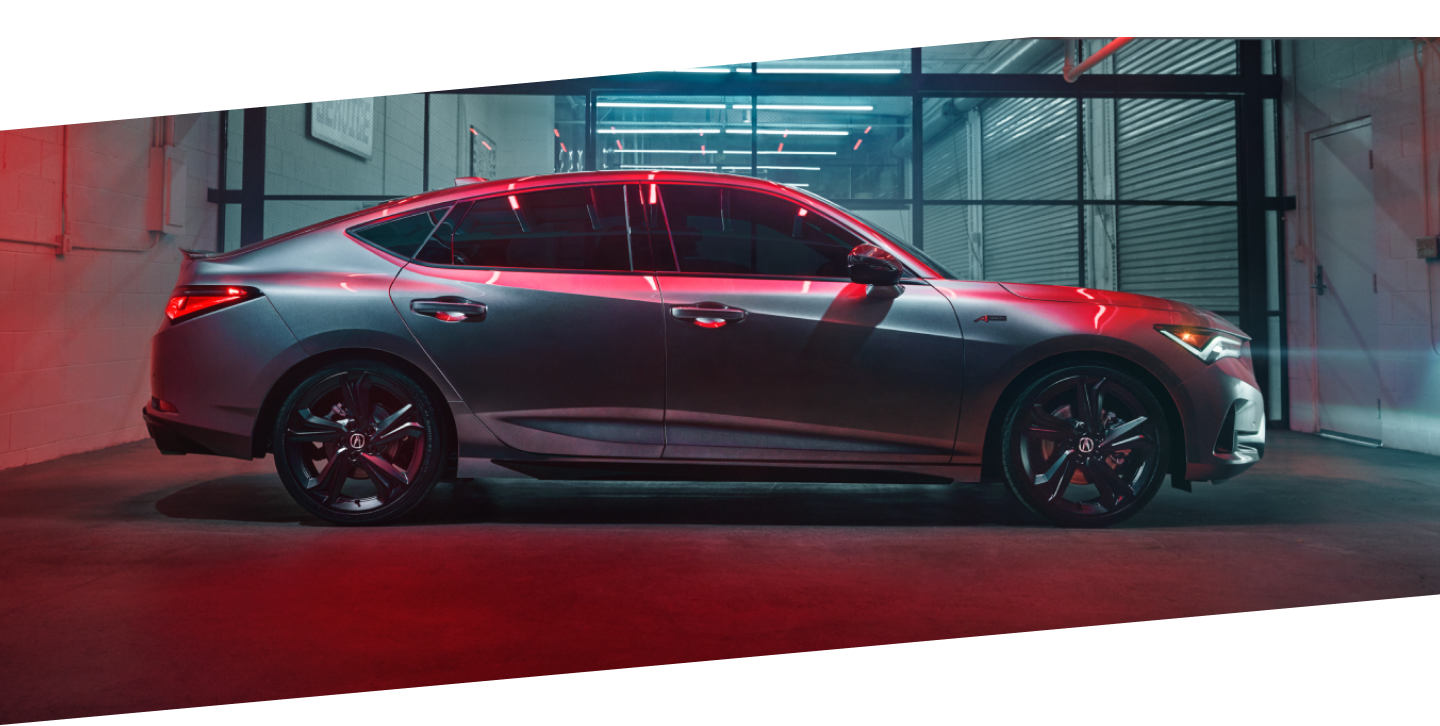 Side view of grey Integra parked in an industrial garage, partly lit by florescent lighting and ambient red light.