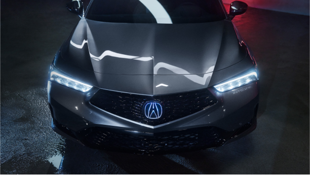 Plan de trois quarts en plongée du capot et du pare-brise d’une Integra grise. L’éclairage fluorescent se reflète sur le capot tandis que la lumière rouge se reflète sur les murs derrière.