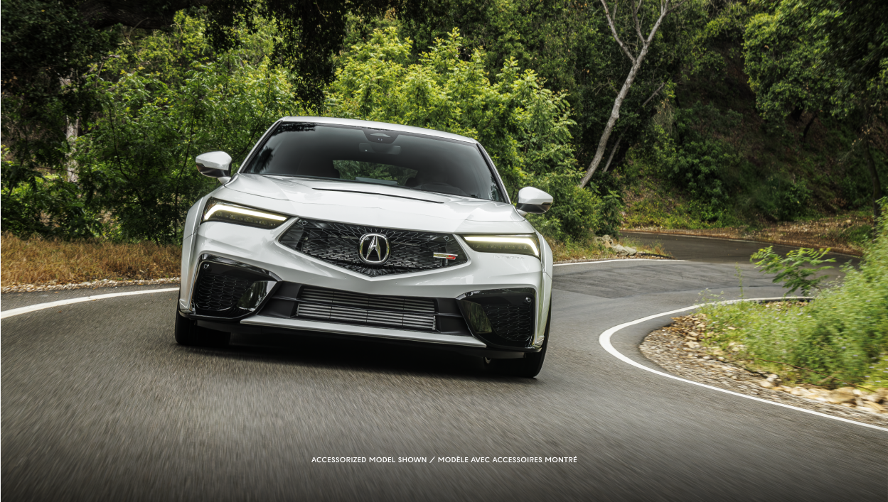 Vue avant d’une Integra blanche roulant sur une route en forêt.