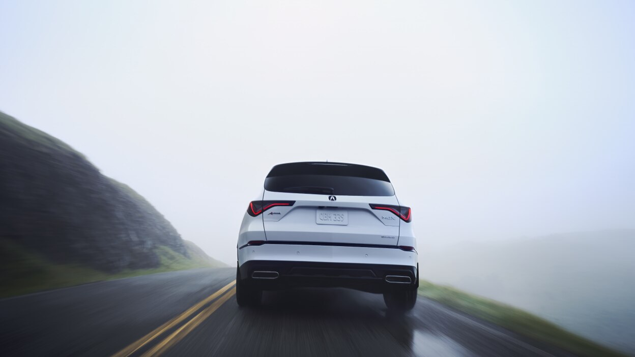 Un MDX gris circulant sous un viaduc en ville.