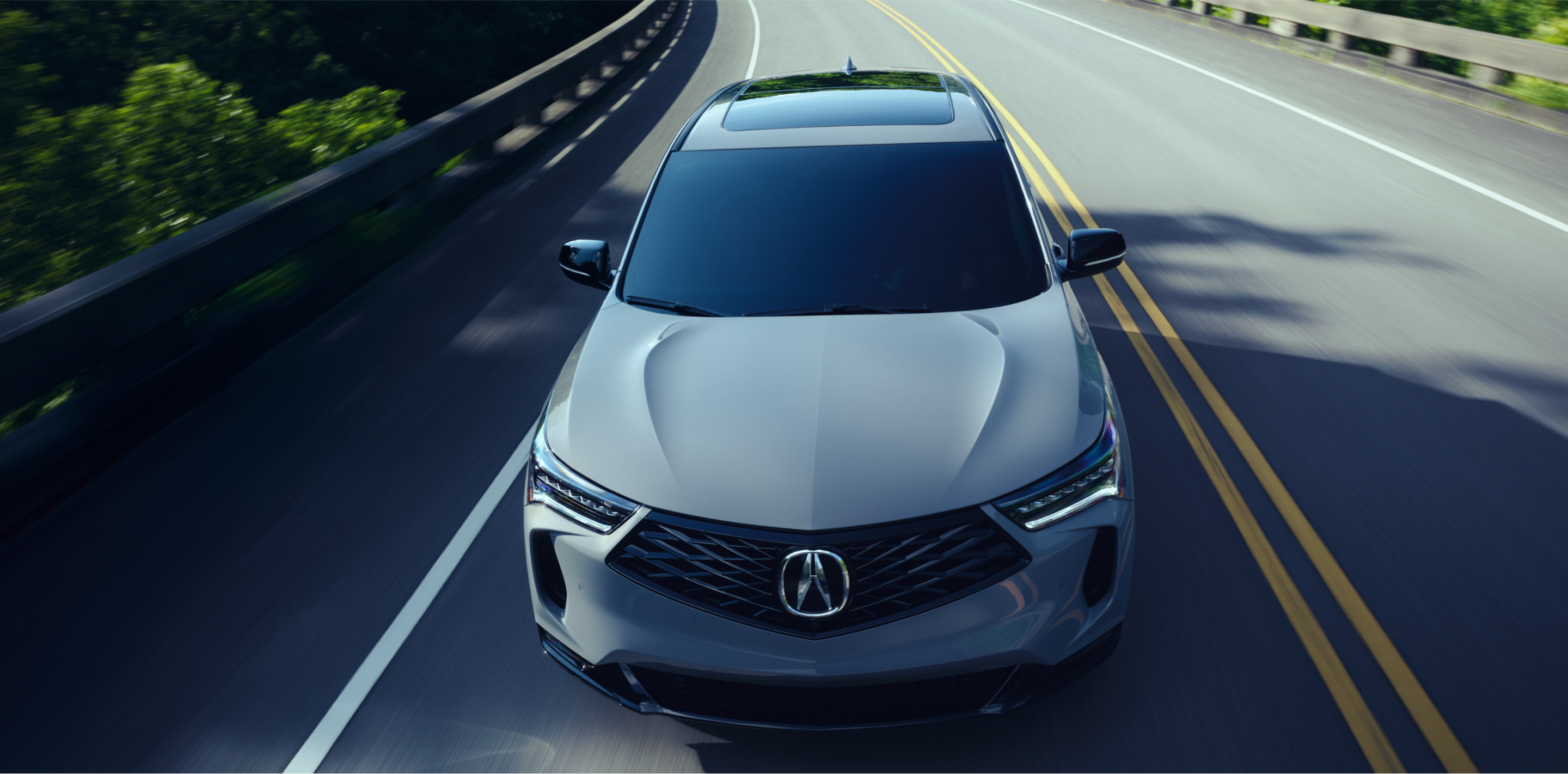 Vue 3/4 en plongée d’un RDX gris circulant sur l’autoroute par une journée ensoleillée.