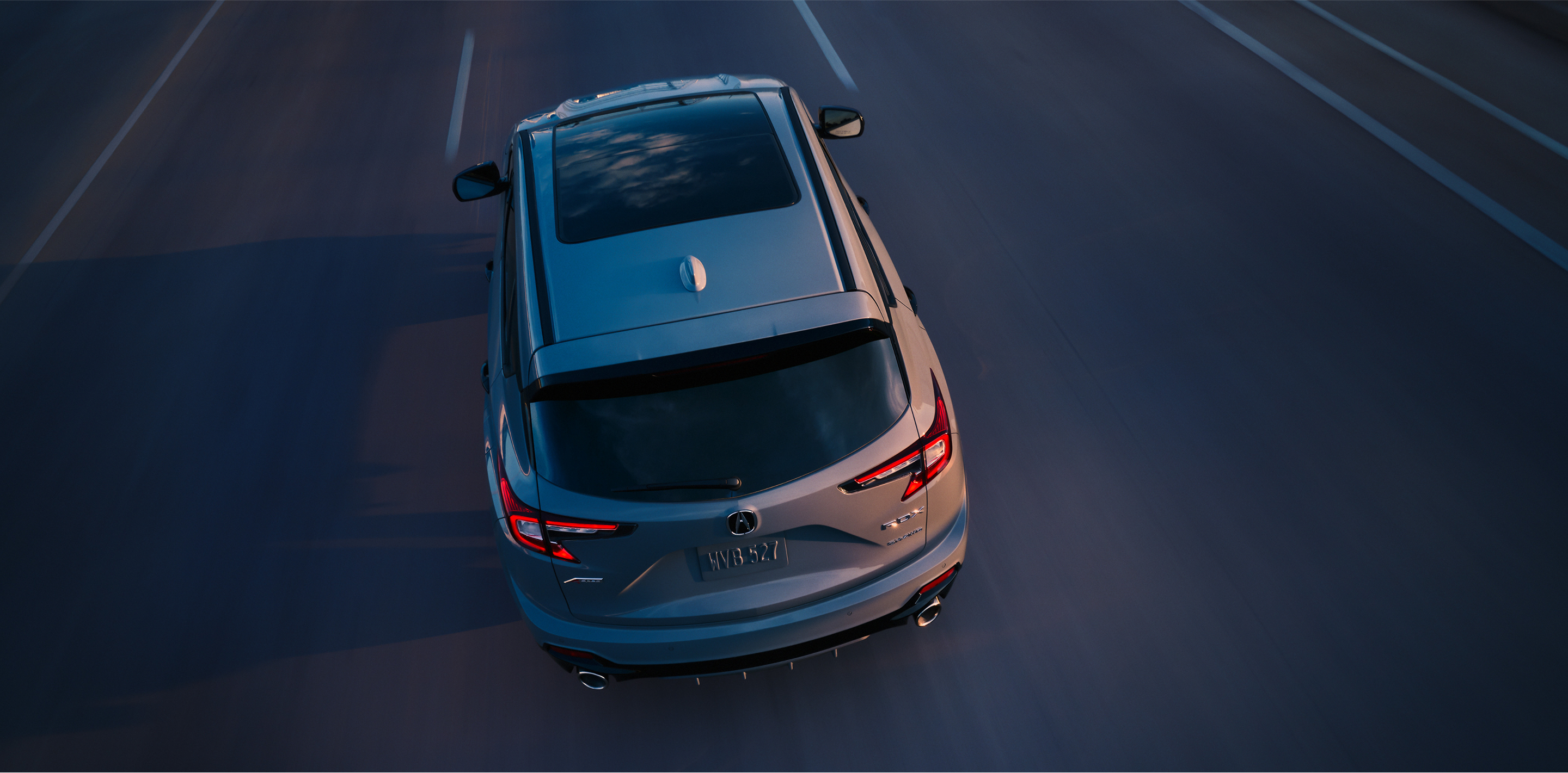 3/4 bird’s eye rear view of grey RDX driving on highway at dusk.