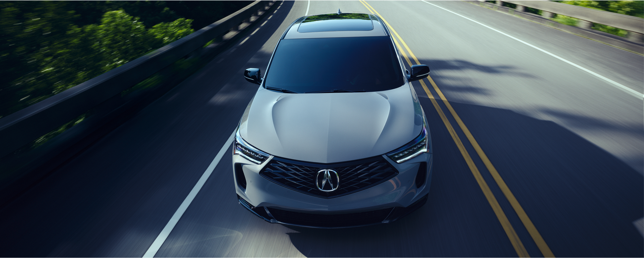 3/4 bird’s eye front view of grey RDX driving on highway on a sunny day.