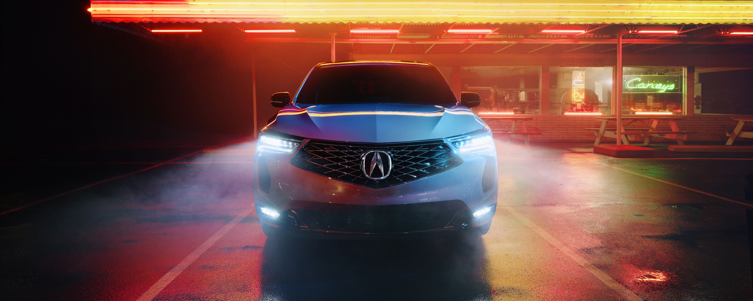 Front view of grey RDX parked in front of a diner with neon lights at night.