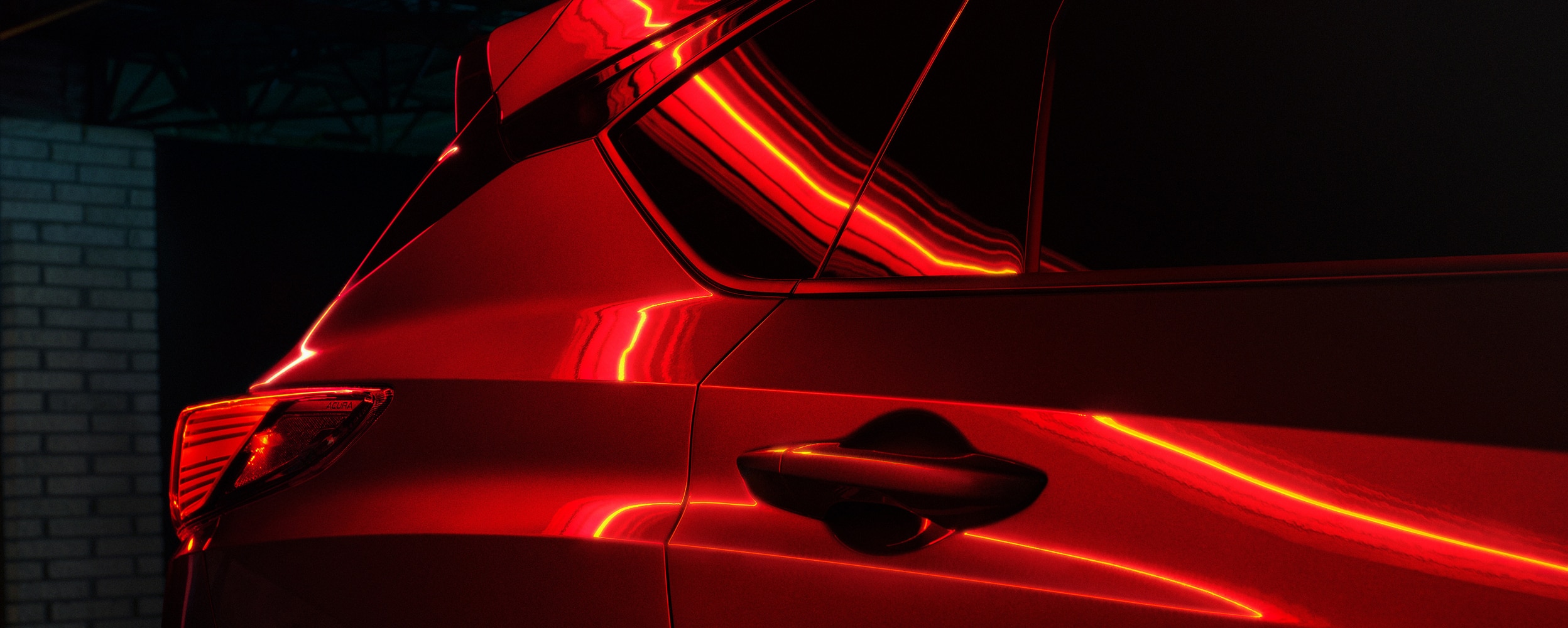 Gros plan sur la porte arrière et sur l’aile d’un RDX éclairé par une lumière rouge.
