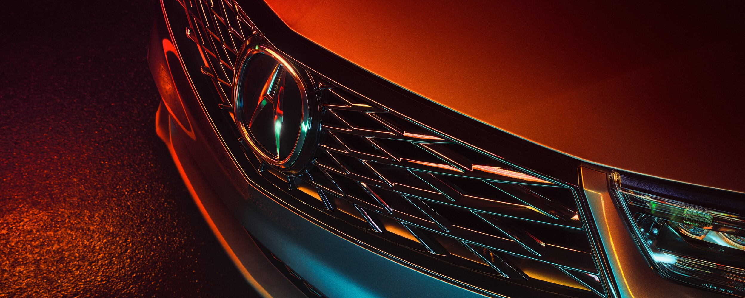 3/4 bird’s eye view closeup of front grill on grey RDX at night, lit by neon lights.