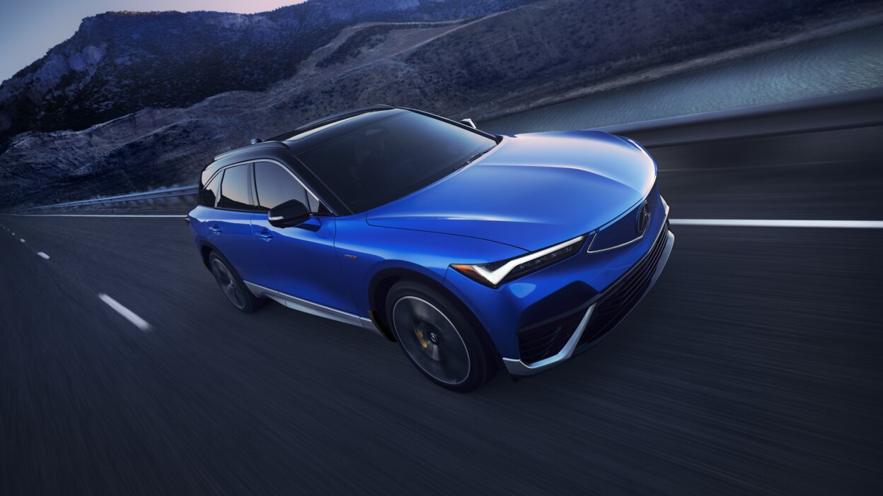 Plan de trois quarts avant en plongée d’un ZDX bleu circulant sur une autoroute désertique au crépuscule.