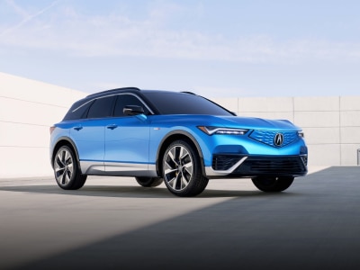 Vue 3/4 avant du ZDX bleu stationné, entouré d'une architecture moderne et minimaliste.