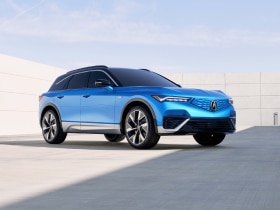 Vue 3/4 avant du ZDX bleu stationné, entouré d'une architecture moderne et minimaliste.