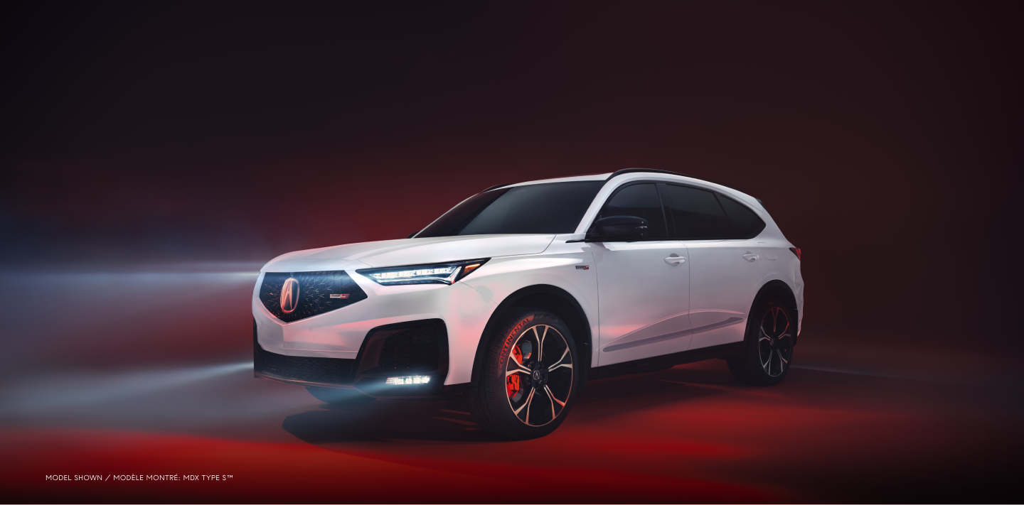 Plan de trois quarts latéral avant d’un MDX blanc avec les phares allumés, dans un studio éclairé par une lumière rouge.