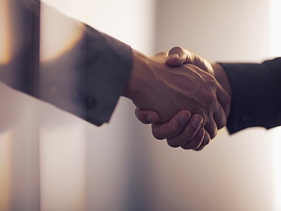 A close-up of two professionally dressed people shaking hands. / Un gros plan de deux personnes en tenue professionnelle se serrant la main.