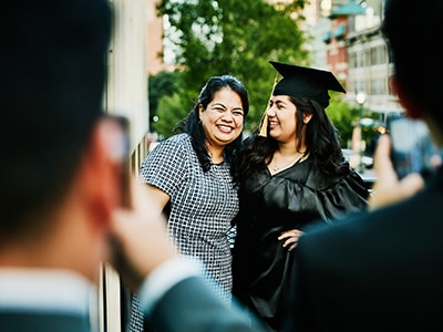 A woman dressed in a graduation cap and gown poses with another woman for a photo. / Une femme vêtue d’un chapeau et d’une toge de graduation posant pour une photo avec une autre femme.