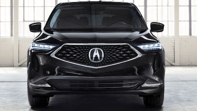 Front-facing shot of a black Acura MDX parked in a large, empty white garage space featuring loft-style windows and white brick walls.	Vue avant d’un Acura MDX noir stationné dans un grand garage blanc vide muni de fenêtres de style loft et de murs de briques blanches.