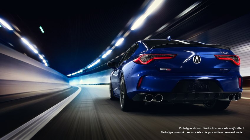 Rear view of a blue Acura TLX driving down a roadway at night, surrounded by city lights blurred by motion.	Vue arrière d’une Acura TLX bleue roulant à pleine vitesse la nuit sur une route bordée de néons.