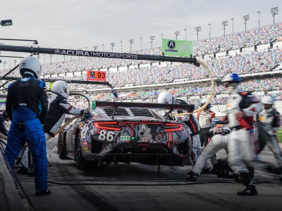 Rear view shot of an Acura NSX GT3 with custom red, white and grey sponsorship graphic wrap. A crew is seen working quickly around the car during a race pit stop. Vue arrière d’une Acura NSX GT3 avec un habillage personnalisé rouge, blanc et gris. Une équipe de ravitaillement travaille rapidement autour de la voiture pendant un arrêt aux puits.