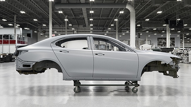 Passenger side view of a white vehicle frame hoisted on a dolly inside the Acura Performance Manufacturing Centre Vue du côté passager d’un cadre de véhicule blanc sur un chariot à l’intérieur du Performance Manufacturing Centre d’Acura.